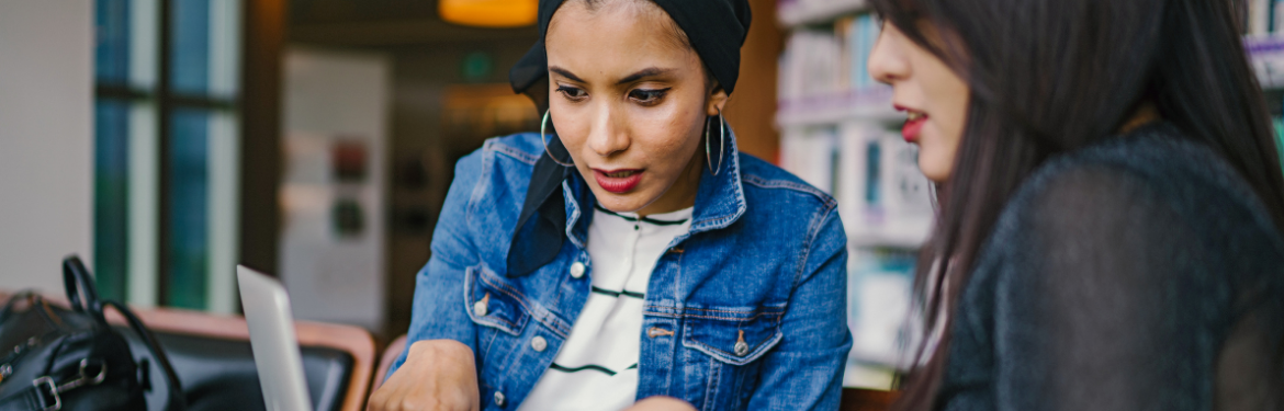 A woman points at a laptop while talking with another woman